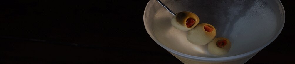 A classic dirty martini is served in a frosted cocktail glass against a dark, dramatic background