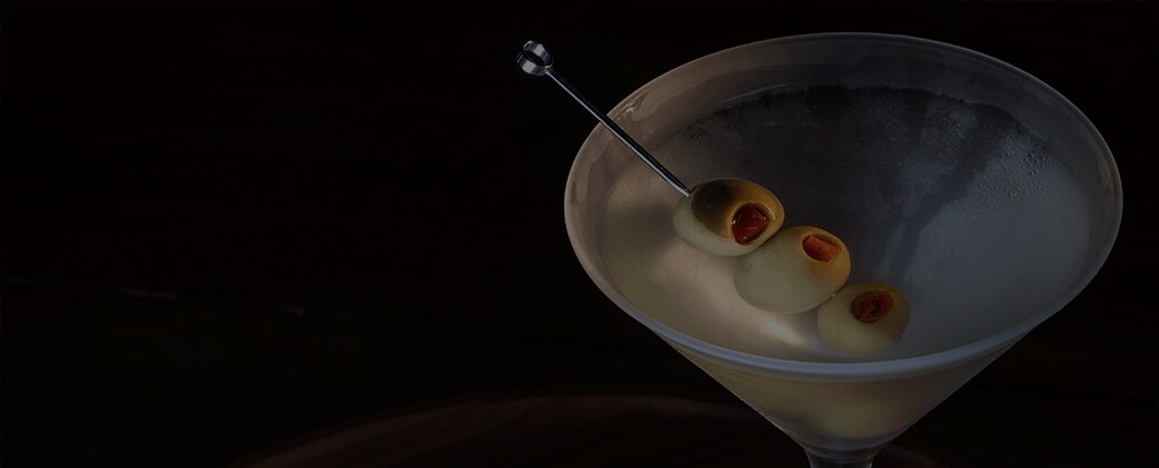 A classic dirty martini is served in a frosted cocktail glass against a dark, dramatic background
