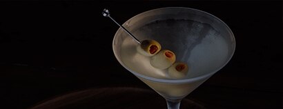 A classic dirty martini is served in a frosted cocktail glass against a dark, dramatic background